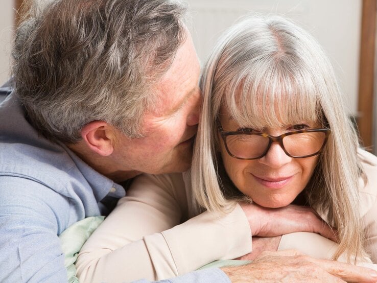 Ein älterer Mann flüstert einer Frau etwas ins Ohr, sie hört gebannt und leicht lächelnd zu