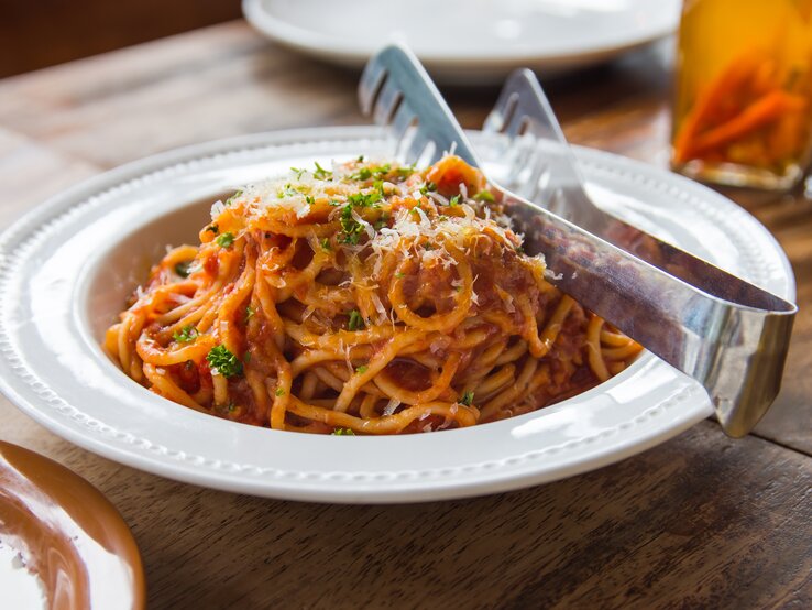 Das Bild zeigt einen Teller mit Spaghetti in einer Thunfisch-Bolognese, bestreut mit geriebenem Käse und etwas gehackter Petersilie. 