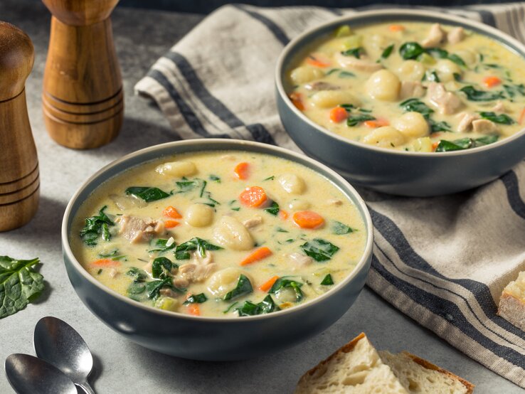Zwei Portionen reichhaltige Suppe mit Huhn, Gemüseeinlage und Brotstück, rustikal serviert.