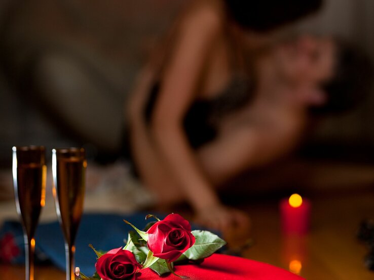 Ein Paar beim Geschlechtsverkehr ist schemenhaft im Hintergrund zu sehen, im Vordergrund stehen zwei Gläser Sekt neben einer Kerze, zwei Rosen liegen daneben 