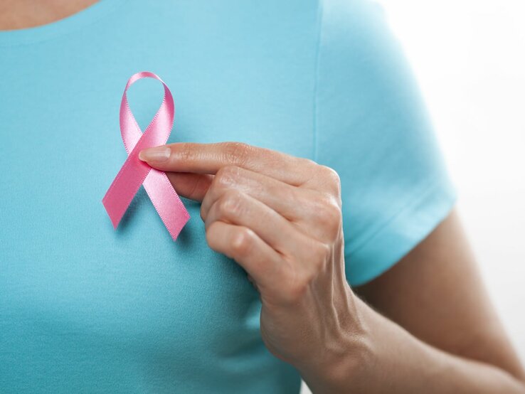 Eine Frau in einem blauen T-Shirt hält eine rosa Schleife vor die linke Brust.
