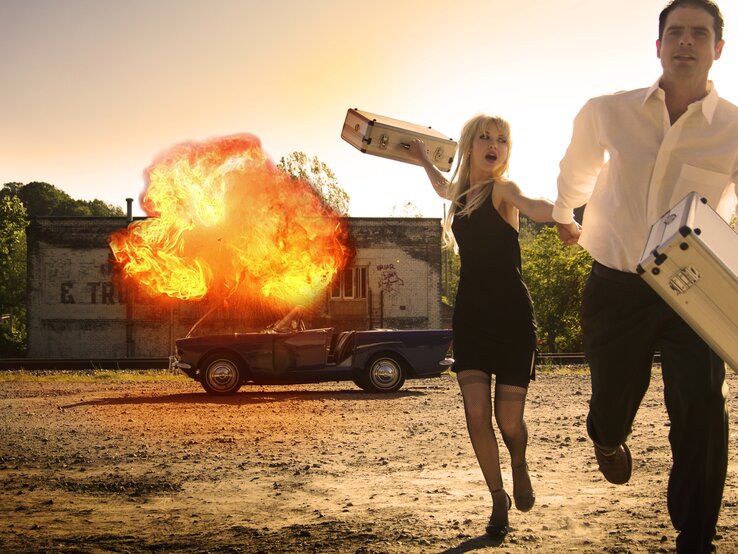 Eine Frau und ein Mann, die vor einem explodierendem Auto fliehen. | © Keith Wright via Gettyimages