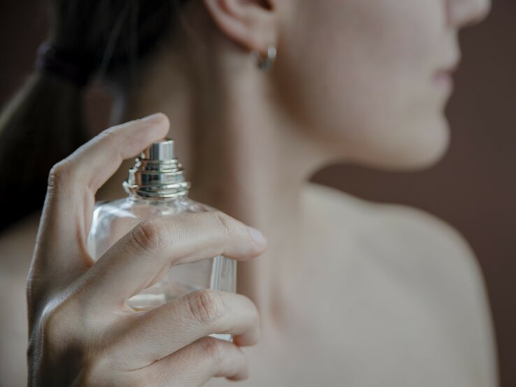  Person sprüht Parfüm auf ihren Hals. Der Fokus liegt auf der eleganten Handhaltung und dem Parfümflakon, während der Hintergrund und der größere Teil der Person unscharf sind. | © iStock.com / tataks