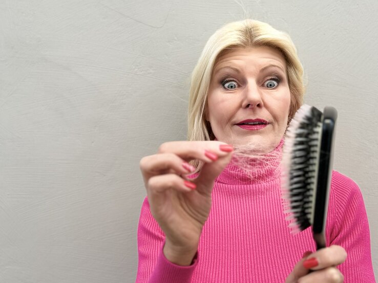 Renate Zott hält eine Haarbürste mit vielen Haaren darin in der Hand und schaut erschrocken darauf | © Renate Zott