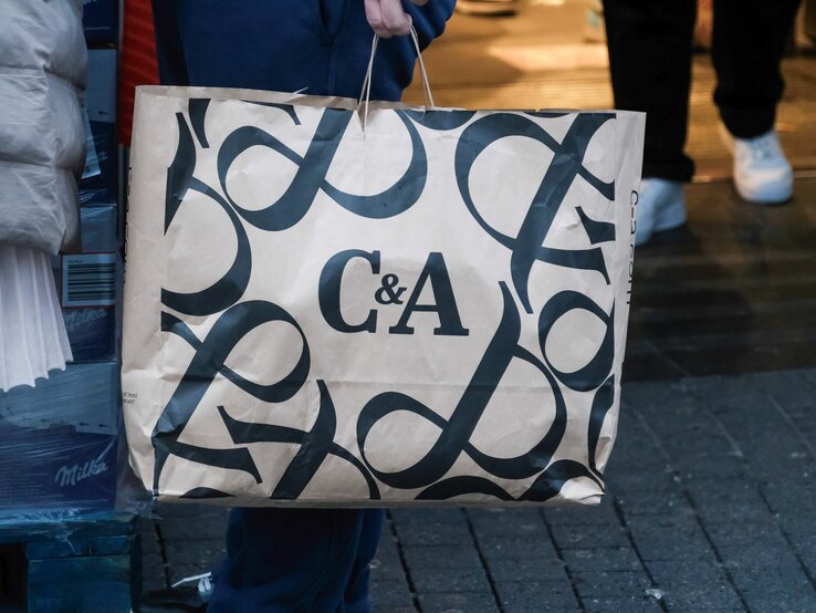 Detailaufnahme einer Einkaufstasche mit C&A-Schriftzug, im Hintergrund unscharfe Passanten.