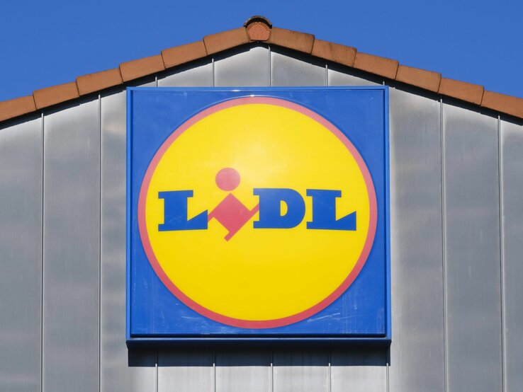 Leuchtendes Lidl-Logo auf blauem Schild, montiert an einer Fassade unter blauem Himmel.