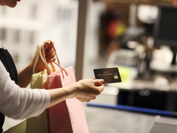 Ein Frauenarm, der Shoppingtüten und eine Kreditkarte hält
