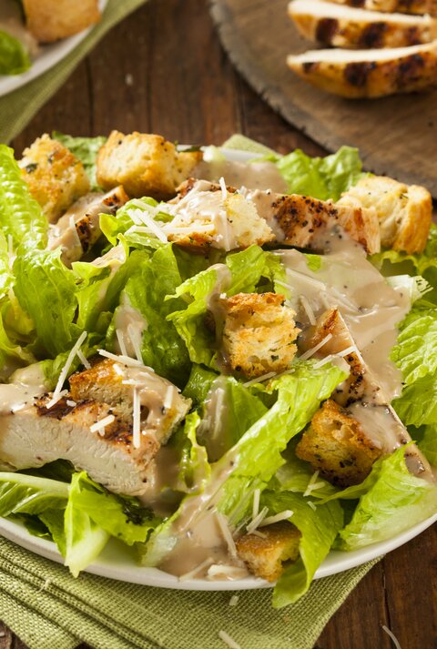 Caesar Salad mit gegrillter Putenbrust und Salatblättern / runder Teller / Gabel / Stoffserviette / angeschnittene Zitrone / Draufsicht, schräg
