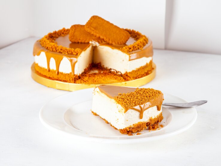 Lotus-Kuchen mit Karamell-Soße Goldene Tortenplatte, darauf ein Käsekuchen mit Lotus-Keksen. Ein Stück wurde herausgeschnitten und auf einem Teller angerichtet.