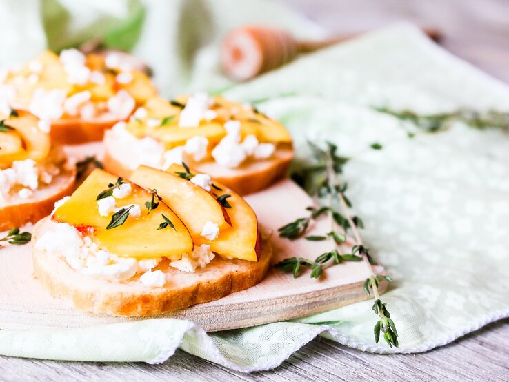 Nektarinen-Feta-Bruschetta auf einem Holzbrett. Daneben einige Zweige Rosmarin. 