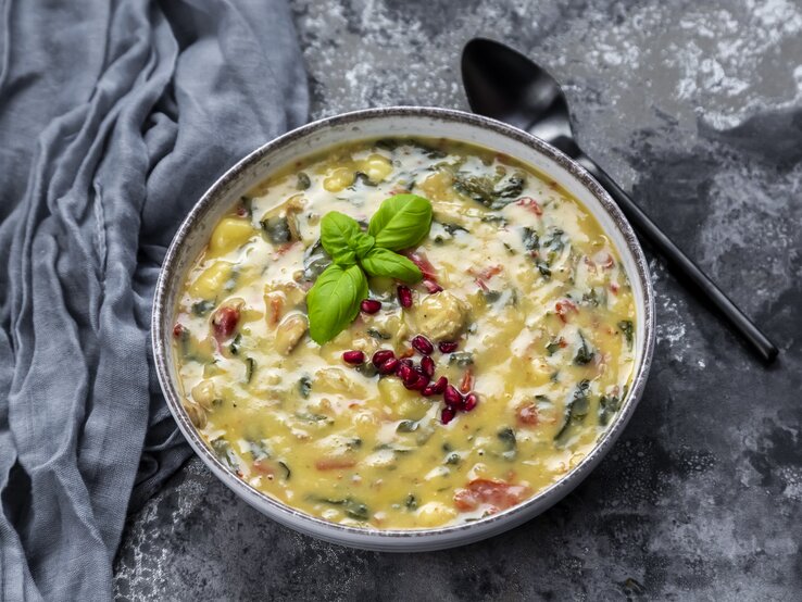 Eine Suppenschüssel mit Gnocchi-Spinat-Suppe auf grauem Hintergrund.