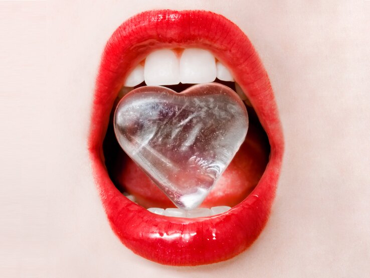Close-up von rote Lippen. Die Zähne halten einen Eiswürfen in Herzform. 