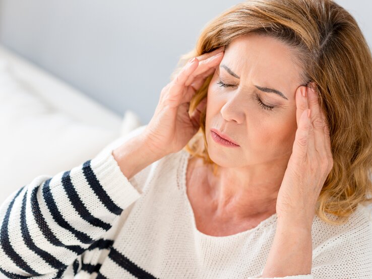 Eine Frau fasst sich bei Kopfschmerzen an die Schläfen und verzieht das Gesicht im Schmerz.