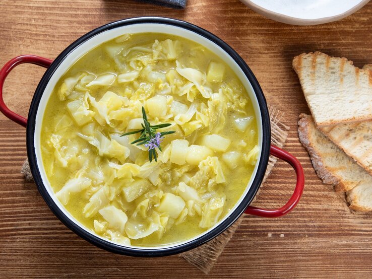 Ein Kartoffel-Weißkohl-Eintopf auf einem Holztisch mit zwei Brotscheiben.