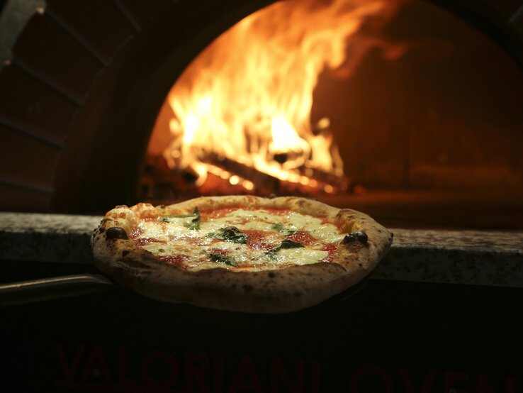 Eine Pizza wird in den heißen Ofen geschoben.  | © iStock.com/Mariha-kitchen