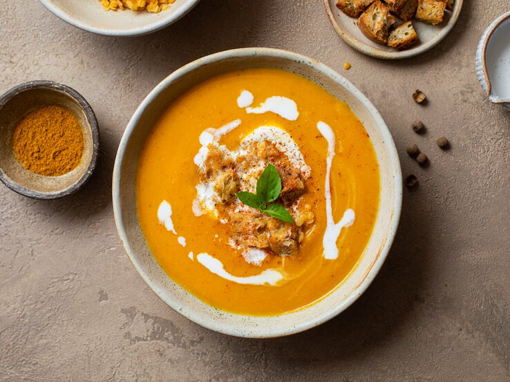Kürbis-Linsen-Suppe in Schale auf hellbraunem Untergrund.