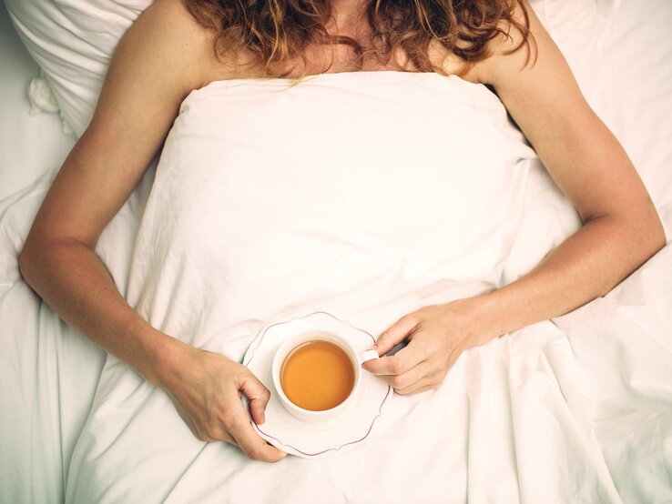 Frau mit einer Tasse Tee liegt im Bett