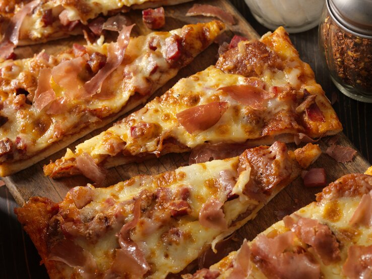 schüttelpizza Pizza-Stücke mit Schinken, Salami und Käse auf Holzbrett.