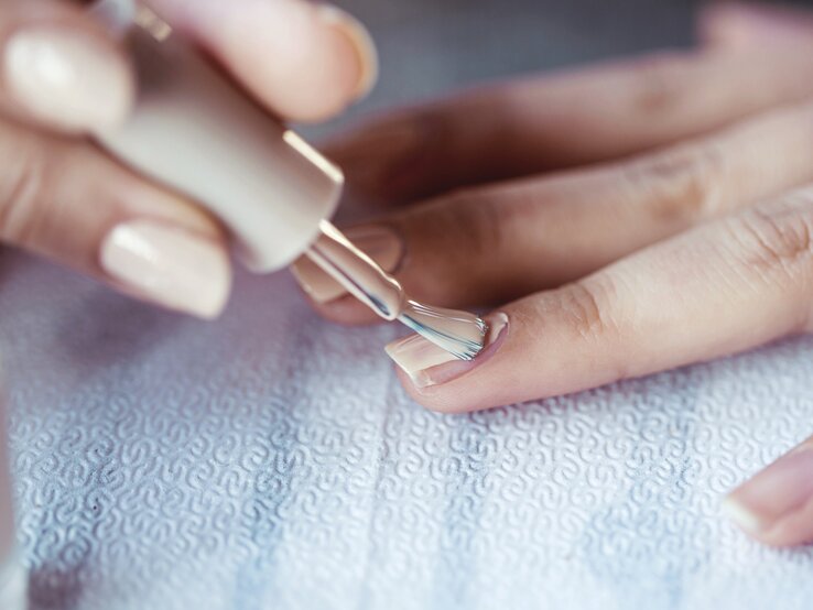 Frau trägt mit der rechten Hand cremefarbenen Nagellack auf die Nägel der linken Hand auf | © iStockphoto.com / Xesai