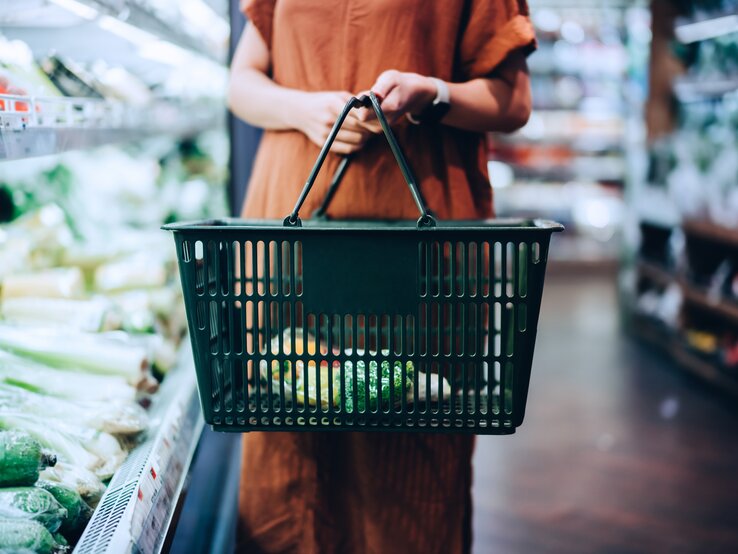 Vegan Food Award 2021: Eine Frau im Supermarkt hält einen Einkaufskorb und steht neben einem Gemüseregal.