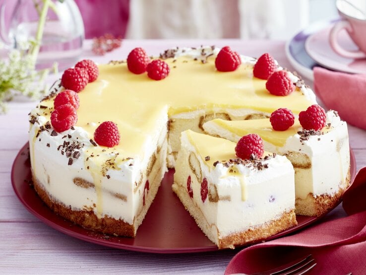 Auf einem Tortenteller steht eine Eierlikör-Himbeer-Tiramisutorte. Sie ist mit Himbeeren und Schokoraspeln dekoriert.