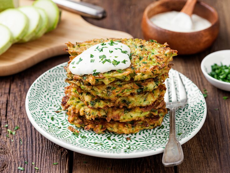Dank eines Klecks Skyr mit Radieschen und Frühlingszwiebeln schmecken die Kartoffelpuffer mit Mangold richtig schön sommerlich. Ein Stapel Kartoffelpuffer mit Mangold und einem Klecks Quark auf einem Teller mit einer Gabel.