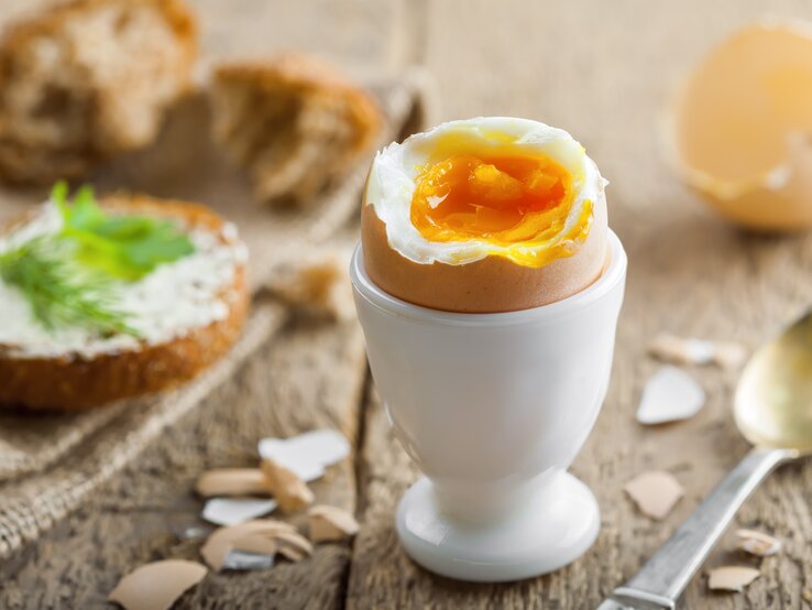 Geköpftes Frühstücksei in weißem Eierbecher auf Holz. 