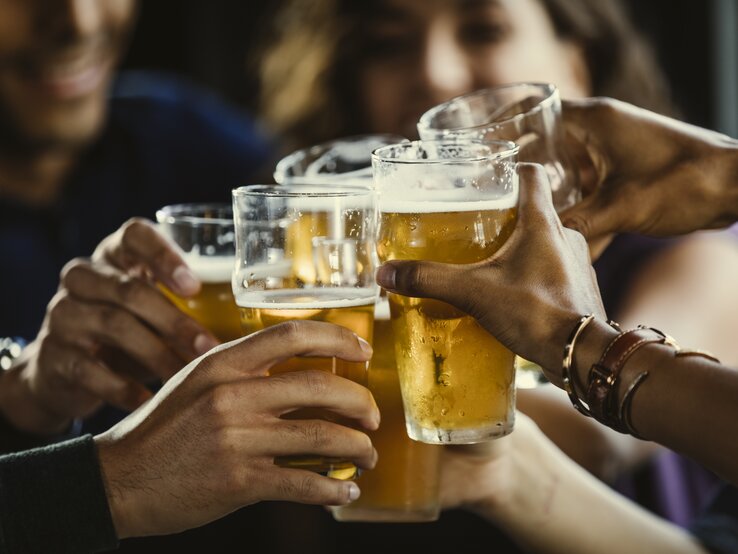 Junge Leute stoßen gemeinsam mit Bier an – in der Mitte sind die Gläser zu sehen