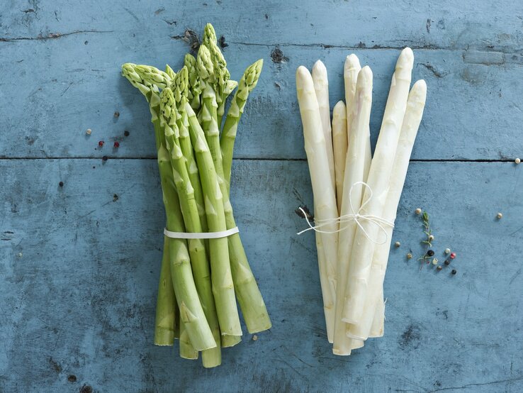 Ein Bund grüner und ein Bund weißer Spargel auf einem blauen Untergrund.  | © GettyImages/Westend61