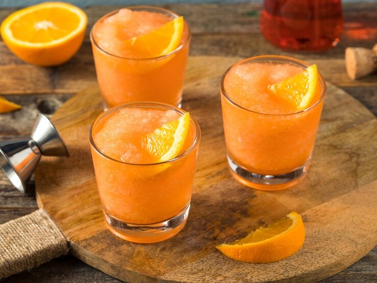 Drei Gläser Frozen Aperol Spritz auf Holzbrett. 