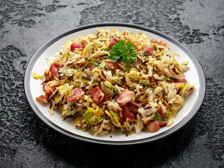 Rosenkohl-Bratreis mit Speck Ein Teller mit Rosenkohl-Bratreis mit Speck auf einem dunklen Untergrund.