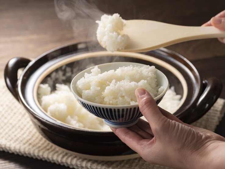 Frisch gekochter, dampfender Reis wird mit einem Löffel vom Topf auf den teller gehoben. 