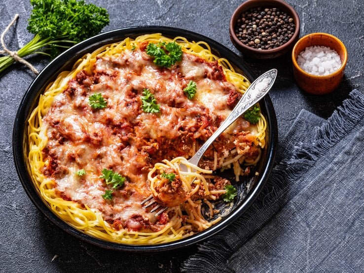 Spaghetti in fruchtiger Hackfleisch-Ricotta-Soße auf schwarzem Teller. Alles auf dunklem Untergrund von schräg oben fotografiert.