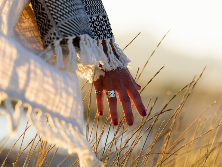 Eine Frau geht im Sommer über ein Feld und streift mit ihren Händen über die Ähren. | © iStock/pepmiba