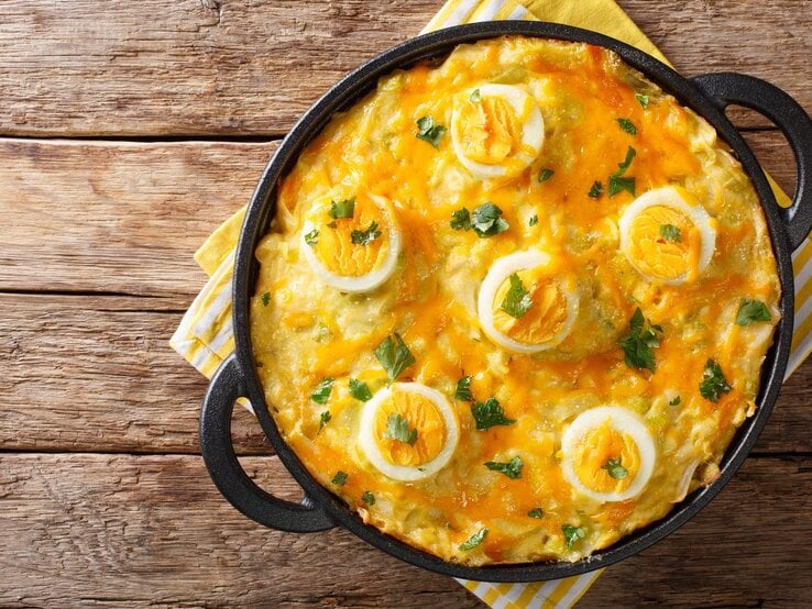 Schon mal walisische, überbackene Eier mit Kartoffelpüree gegessen. Heißen dort Anglesey Eggs und schmecken fantastisch. Anglesey Eggs in gusseiserner Pfanne auf hölzernem Untergrund.