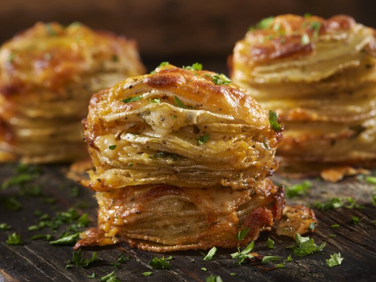 Käsige Kartoffelstapel mit Petersilie bestreut auf einem Holzbrett. 