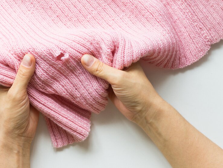 Ein rosa Pullover hat ein kleines Loch.