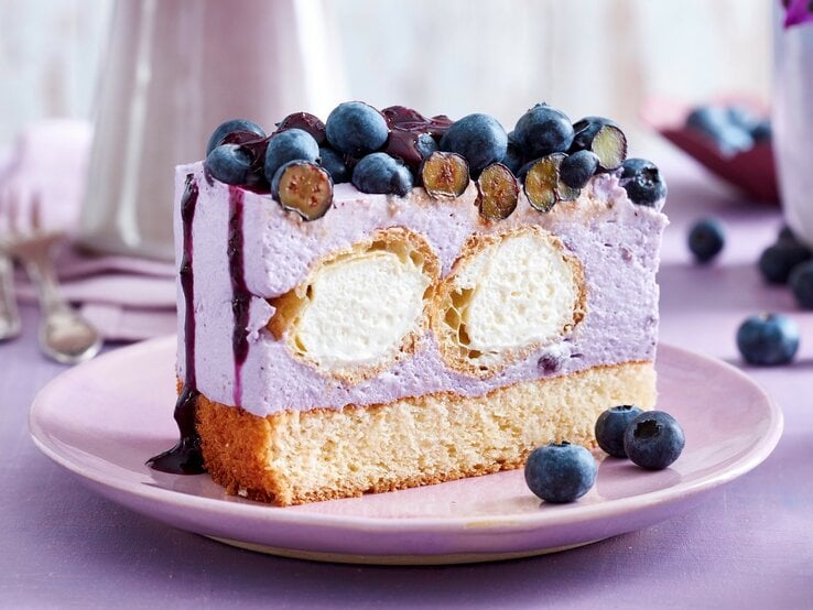 Auf einem Teller steht ein Stück Windbeutel-Joghurt-Torte. Es ist mit Blaubeeren und Soße verfeinert. Im Inneren befinden sich zwei Windbeutel. | © EAT CLUB / Isabell Triemer