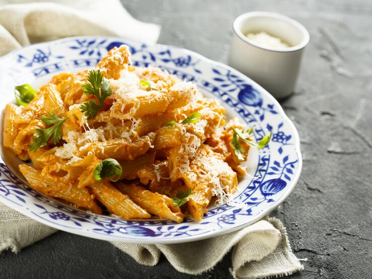 Altmodischer Teller belegt mit penne in Paprika-Sahne-Soße – bestreut mit geriebenem Parmesan und Petersilie. 