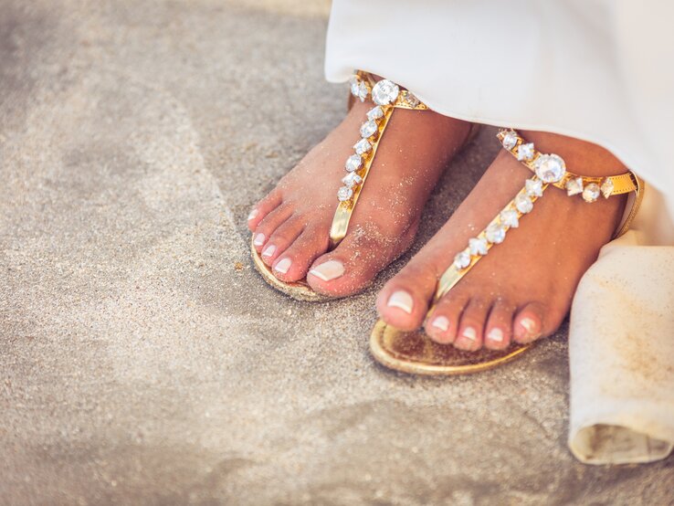 Frauen Füße auf Sandstrand mit Sandalen.