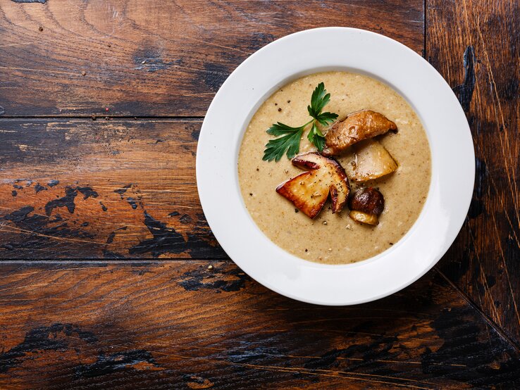 Steinpilzsuppe Draufsicht auf einen weißen teller mit cremiger Steinpilzsuppe. Das Ganze steht auf einem dunklen Holztisch.