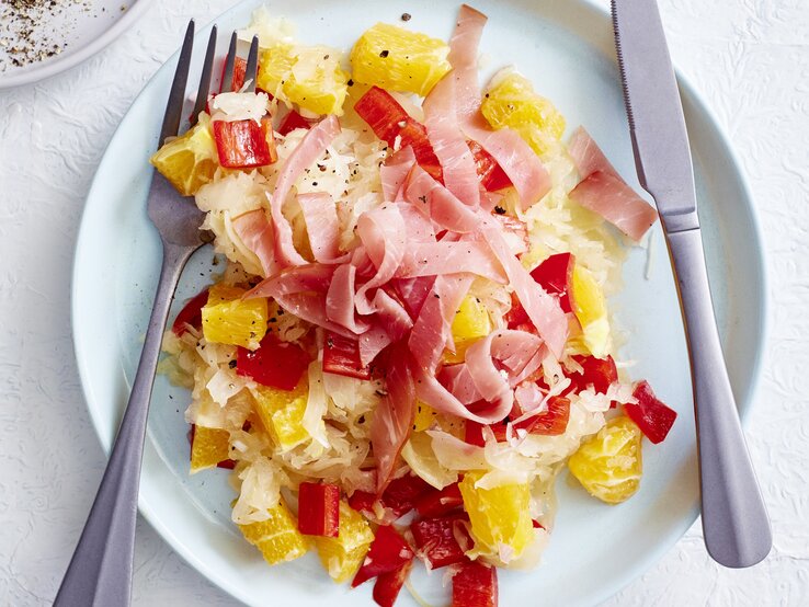 Appetit auf eine köstliche Mahlzeit für zwischendurch? Dann verpasse nicht unser neues Rezept für Sauerkrautsalat mit Orange. Sauerkrautsalat mit Orange und Schinken auf Teller angerichtet.