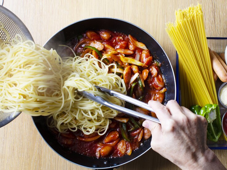 Spaghetti werden aus einem Sieb in eine tomatige Gemüsesoße gekippt.