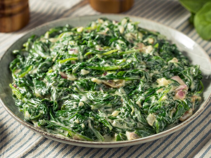 Eine Schüssel mit cremigem Spinat auf einer blau-weiß gestreiften Tischdecke.