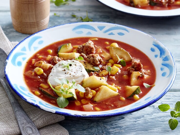 Unser deftige Zucchini-Tomaten-Eintopf mit Hack schmeckt besonders gut mit etwas Brot dazu. Probieren Sie es aus! Auf einem tiefen Teller ist eine Portion Zucchini-Tomaten-Eintopf mit Hack serviert. Sie wird mit Frischkäse verfeinert.