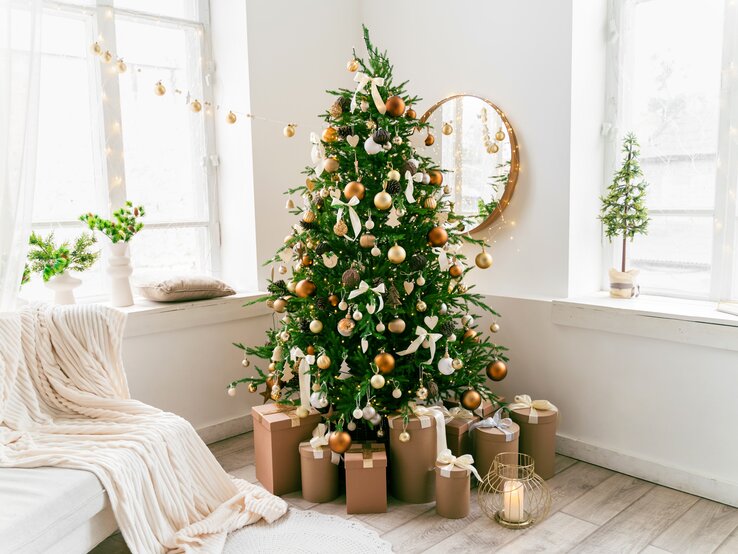 Weihnachtsbaum mit goldenen Kugeln steht im Wohnzimmer. Auch die andere Weihnachtsdeko ist in Gold gehalten. 