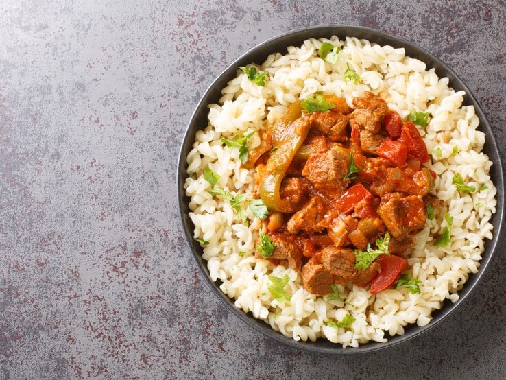 Draufsicht: Runde Schüssel / gekochte Nudeln und Gulasch. Es handelt sich um den ungarischen Rindfleisch-Eintopf Pörkölt.