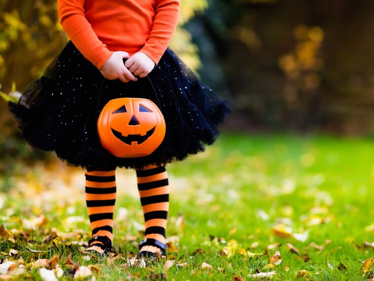 Kleines Mädchen, der Kopf ist nicht zu sehen, in schwarz-orangenem Halloween-Kostüm