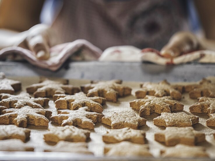 Frau zieht ein Backblech belegt mit sternförmigen Plätzchen aus einem Backofen. 