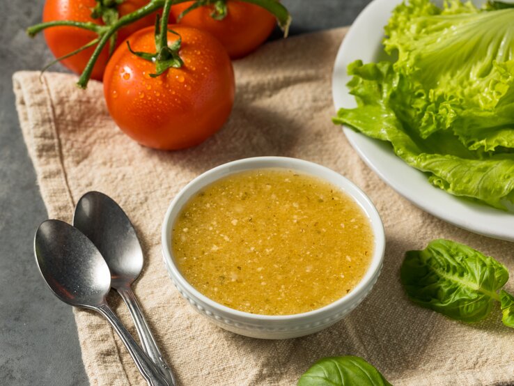 italienisches Knoblauchdressing in kleiner Schale. Daneben Tomaten und Blattsalat. 